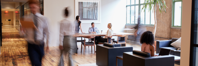 Office workers in a modern, open-plan workspace with a mix of seated collaboration and movement.